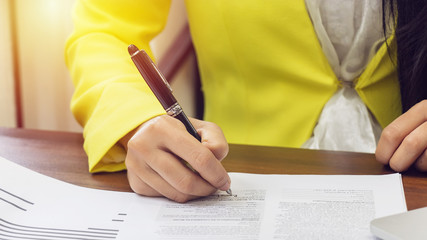 business women in yellow suite use pen sign the signature of consent in the contract agreement document. business partnership and legal agreement of lawyer concept