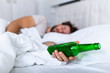 Unconscious drunk man with bottle of alcohol in hands sleeping in bed . Alcoholism problem and hangover concept
