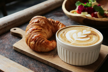 Wall Mural - A cup of coffee with latte art on top, butter  croissant and granola with fresh tropical fruits and yogurt on table in caffee. Concept of healthy breakfast