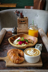 Wall Mural - A cup of coffee with latte art on top, butter  croissant and granola with fresh tropical fruits and yogurt on table in caffee. Concept of healthy breakfast