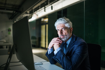 Wall Mural - Portrait of mature businessman with computer in an office, looking at camera.