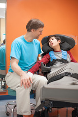 Disabled little boy in wheelchair talking with father in hospital room