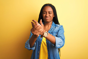 Canvas Print - Young african american woman wearing denim shirt standing over isolated yellow background Suffering pain on hands and fingers, arthritis inflammation