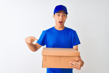 Wall Mural - Chinese deliveryman wearing cap holding box standing over isolated white background very happy pointing with hand and finger