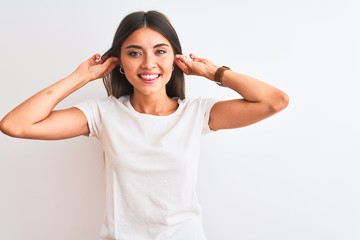 Wall Mural - Young beautiful woman wearing casual t-shirt standing over isolated white background Smiling pulling ears with fingers, funny gesture. Audition problem