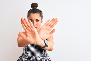 Wall Mural - Beautiful woman with bun wearing casual dresss standing over isolated white background Rejection expression crossing arms and palms doing negative sign, angry face