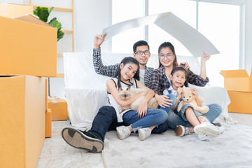 asian family relax and sitting on floor near sofa, they moving to new resident, they feeling happy and smile in family time, asian father and mother up paper roof above his head, home sign with hand