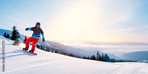 Fototapety Sporty Zimowe  mlody-snowboardzista-jazda-na-czerwonym-snowboardzie-w-gorach-w-sloneczny-dzien-snowboard-i-zima