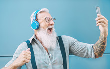 Happy Senior Man Taking Selfie While Listening Music With Headphones - Hipster Mature Male Having Fun Using Mobile Smartphone Playlist Apps - Technology And Elderly Lifestyle People Concept