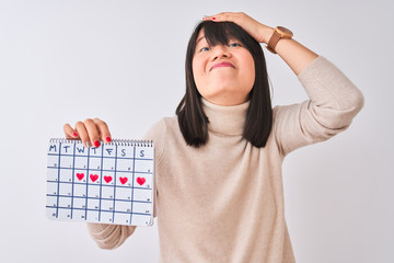 Wall Mural - Young beautiful Chinese woman holding menstruation calendar over isolated white background stressed with hand on head, shocked with shame and surprise face, angry and frustrated. Fear and upset 