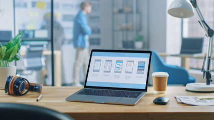 Poster - Shot of Laptop Standing at Desk in the Creative Office. Notebook Screen Shows Mobile Phone Application Design, Software UI Development. In Background Young Professional Stans in Creative Modern Office