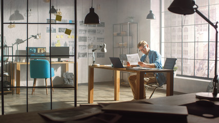 Poster - Professional Creative Designer Works on a Laptop in Loft Office, Looks at the Product Sketches and Concepts He Has Drawn. Stylish Design or Gaming Content Development Studio. Golden Hour Shot