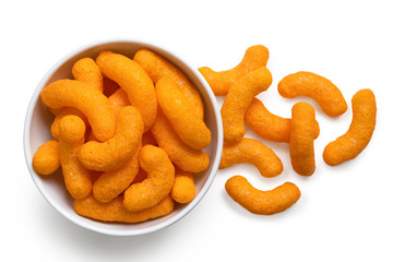 Wall Mural - Extruded cheese puffs in a white ceramic bowl next to spilled cheese puffs isolated on white. Top view.