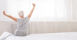 Well slept senior woman stretching with arms raised on bed