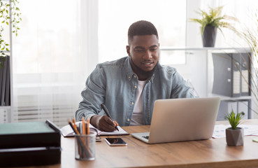 Poster - Young businessman using laptop and taking notes at worklace in office