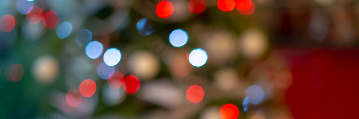 Panoramic web banner of blurred green and red bokeh holiday lights at night, christmas tree background