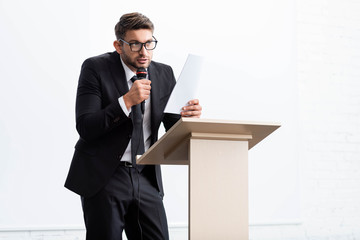 Wall Mural - scared businessman in suit standing at podium tribune and speaking during conference isolated on white