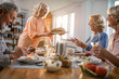 © Drazen - Happy senior woman serving bread to her friends during lunch time at home.