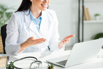 cropped view of smiling doctor having online consultation with patient on laptop in clinic office