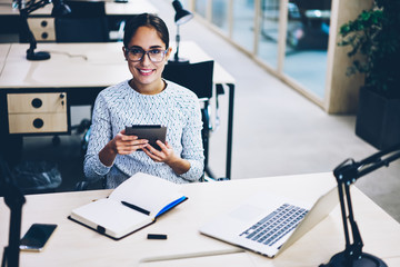 Portrait of cheerful female employee satisfied with good news about successful project checking notification on tablet, skilled administrative manager using portable pc for organizing job in office