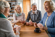 © Drazen - Group of happy seniors laughing while playing cards together at home.