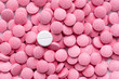 Pile of pink pills and around a white one. Medication, self-treatment or placebo concept: one tablet is different from the lot of others