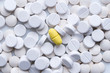 Pile of white pills and around a yellow one. The concept of different, alternative or placebo treatment