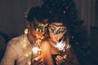 © maryviolet - Christmas and New year party concept. Couple in love burning sparklers by illuminated Christmas tree with champagne.