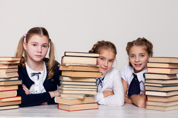 three girls of school girls with books for study sit at the desk in the classroom