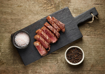 Wall Mural - Sliced grilled beef steak with salt and pepper on wooden background