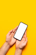 © olgaarkhipenko - Male hands hold a modern black smartphone with white blank screen on yellow background. Modern technology, phone, gadget in hands, touch screen, template for your design. Mockup