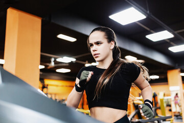 Portrait of a young charming attractive woman professional coach running on a treadmill in a gym. Concept of discipline and endurance as a path to success