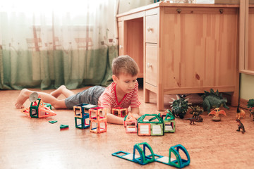 A boy plays with dinosaurs and magnetic constructor in a children room laying on cork floor
