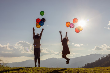 Two children jumping playing with colored balloons at sunset.