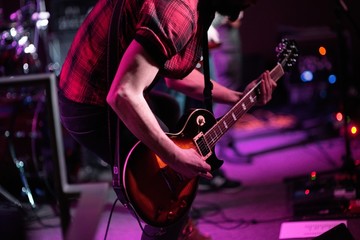 Rock band performs on stage. Guitarist, bass guitar and drums. The guitarist plays.