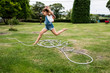 © Mint Images - Girl jumping over hose in lawn