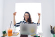 © BullRun - Joyful young businesswoman sitting at table with hands up