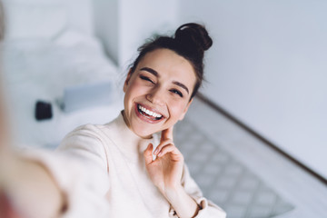 Wall Mural - Attractive young woman using camera of smartphone taking sunny selfie at home