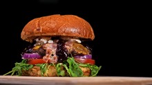 Craft Burger Is Cooking On Black Background. Consist: Sauce, Arugula, Tomato, Red Onion, Bacon, Red Currant Sauce, Ricotta Cottage Fresh Cheese, Air Bun And Marble Meat Beef. Not Made Ideal. Looks