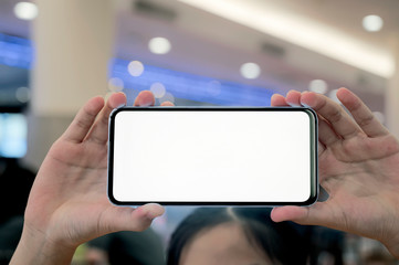 Wall Mural - Shot of female hand holding and showing blank screen smartphone in horizontal view while standing at shoppping mall.