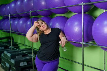 Wall Mural - Woman drink water after intense training in a sports club. Fat blonde is resting in the gym between sets.