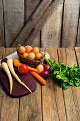 Poster - basket of eggs and tomato, spanish onions, carrots, parsley roots, celery, cutting board, old weathered wooden table background