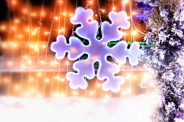 Wall Mural - snowflake christmas new year decoration of winter wonderland city street at night against garland lights background. Side view of town street light and christmas tree branches in snow. Creative blur