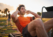 © StratfordProductions - Confident young man listening to music in headphones from smart phone armband doing exercises on public equipment in the outdoor gym at the park
