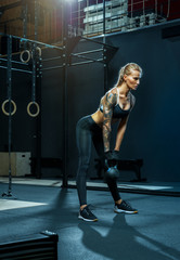 Attractive confident athletic woman cross-fit exercising with kettlebell while being in squat position Muscular woman doing kettlebell swing routine crossfit workout at gym Strong caucasian woman