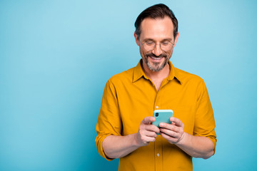 Portrait of cheerful attractive mature man modern device user use his smart phone type social network message wear good looking clothes isolated over blue color background