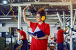© Dusan Petkovic - Smiling Caucasian cute young female employee with antiphons on ears holding notebook, monitoring other employees and waving.