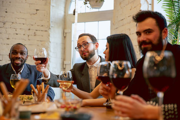 Wall Mural - Happy co-workers celebrating while company party, corporate event. Young caucasian people in business attire talking, drinking wine. Concept of office culture, teamwork, friendship, holidays, weekend.