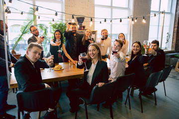 Wall Mural - Happy co-workers celebrating while company party and corporate event. Young caucasian people in business attire cheering, laughting. Concept of office culture, teamwork, friendship, holidays, weekend.