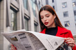 Cute smart concentrated charming lady in black golf and a red autumn coat in earrings rings reads fresh newspaper